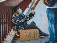 Young homeless man with cardboard sign receiving money donation